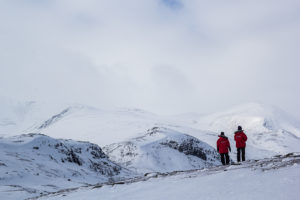 Två personer beundrar utsikten i fjällen vintertid. Foto från turen Smak av Sarek med hundspann